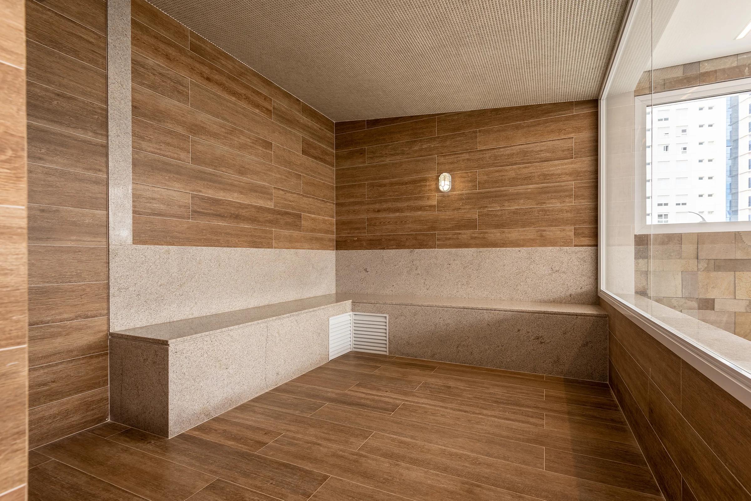 Sauna revestida com porcelanato amadeirado e bancos de pedra
