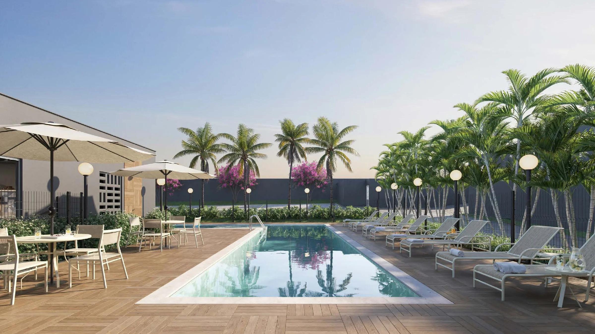 Deck da piscina com espreguiçadeiras, mesas com ombrelone e palmeiras
