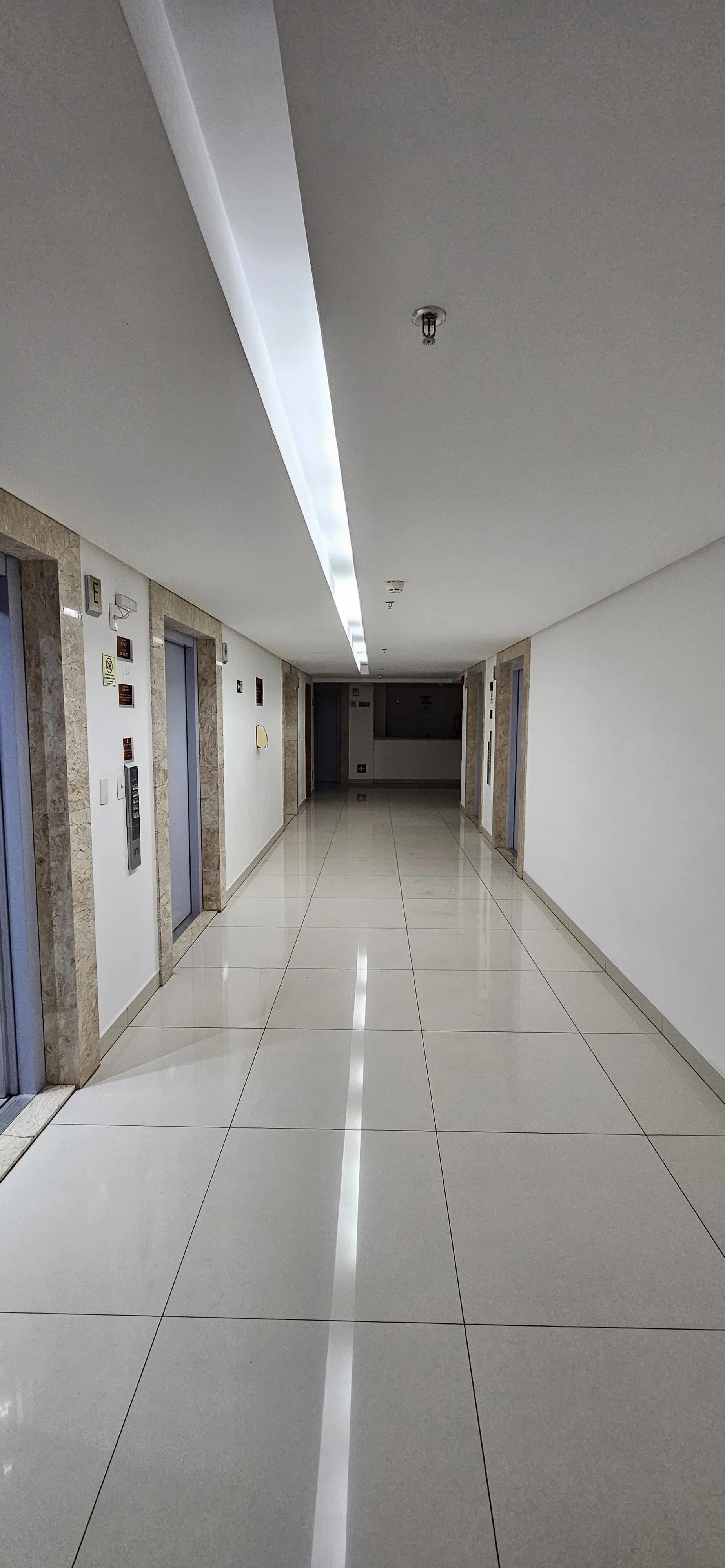 Corredor interno de circulação e hall de elevadores com piso em porcelanato claro