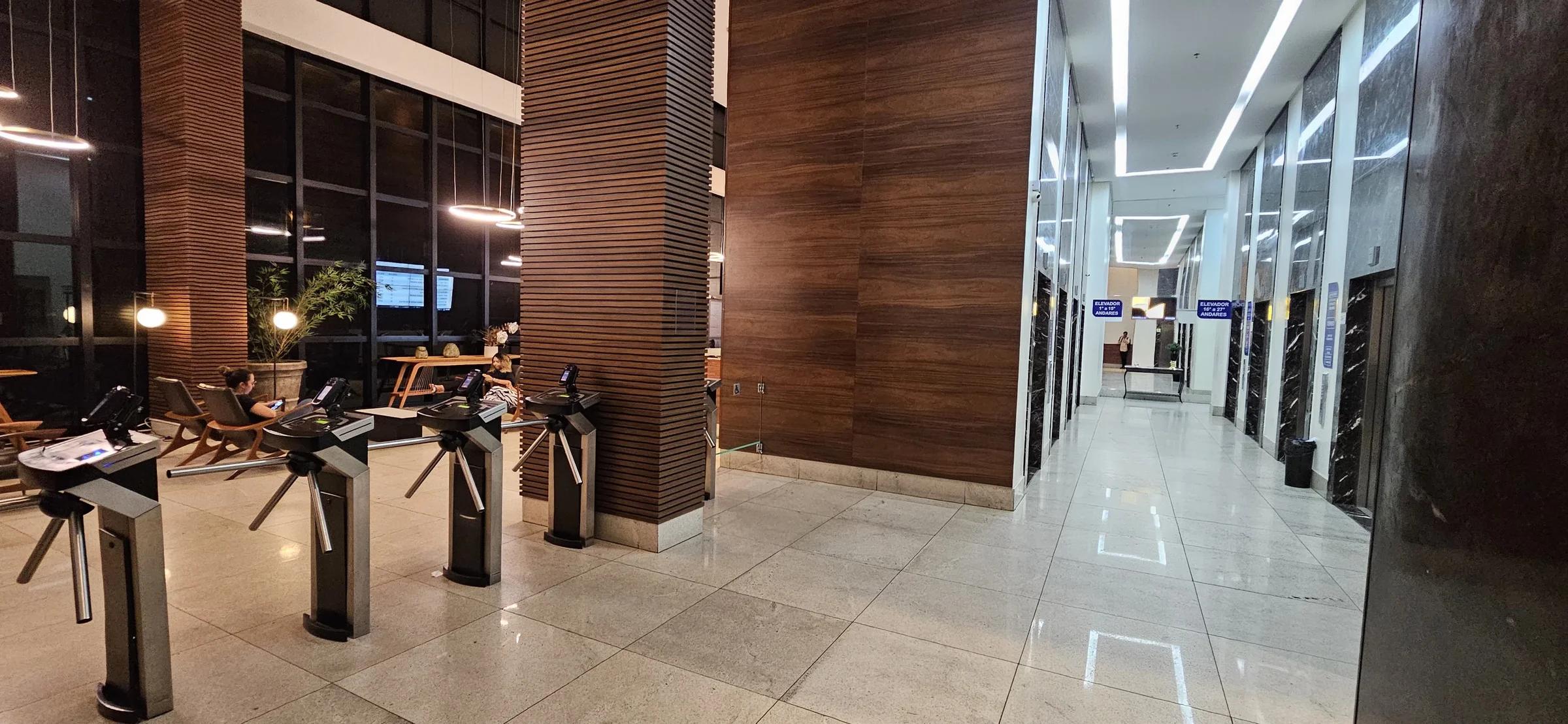 Lobby principal do edifício com controle de acesso por catracas eletrônicas e pé-direito duplo