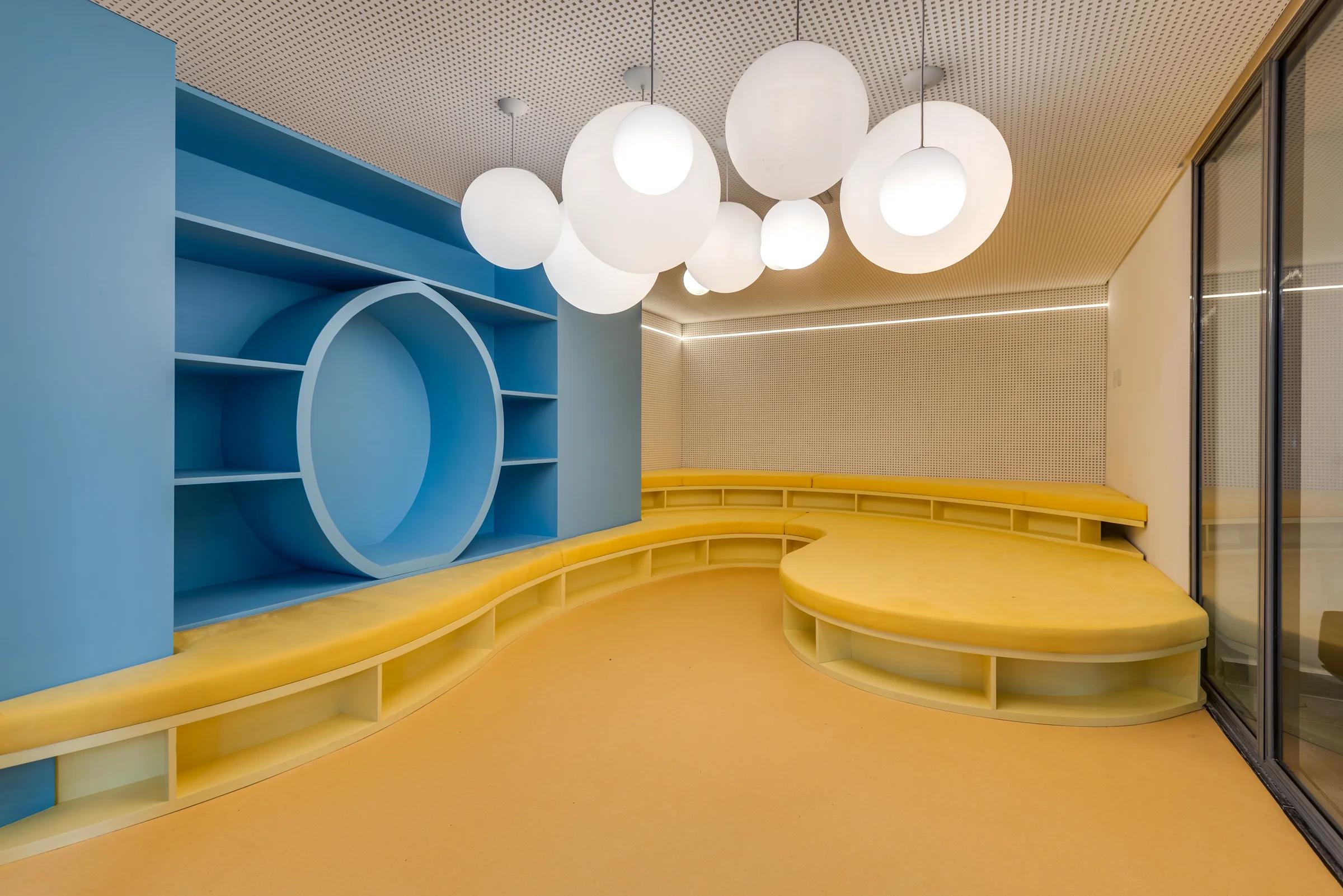 Foto de espaço infantil interno com estante azul e mesa amarela.