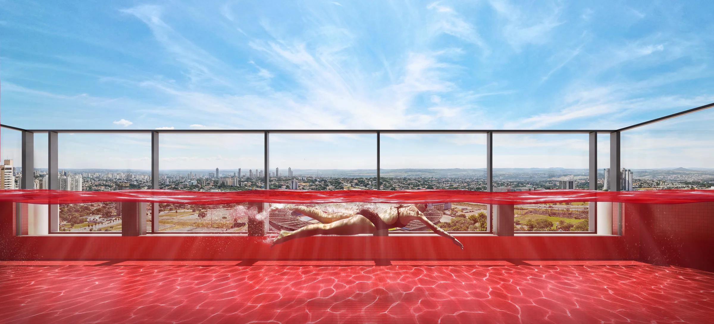 Piscina vermelha no rooftop com parede de vidro e vista panorâmica para a cidade durante o dia