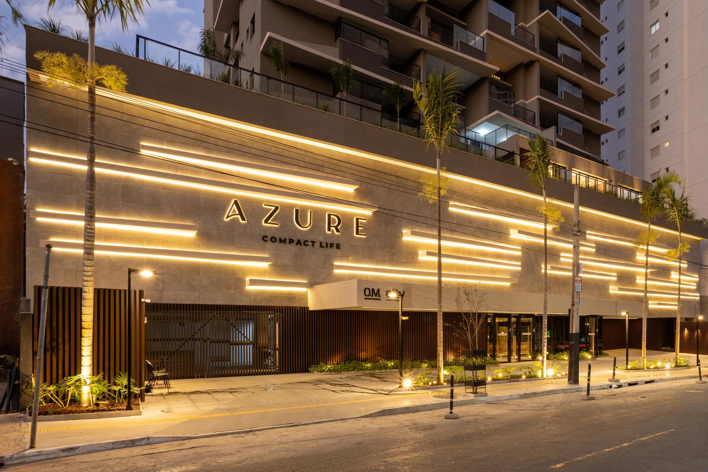 Fachada do Azure Compact Life à noite com letreiro iluminado e fita de luz no embasamento